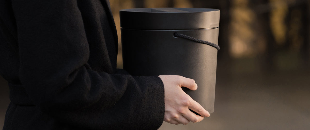 Person holding a black Kaarna urn by Nautrn with a blurred natural background